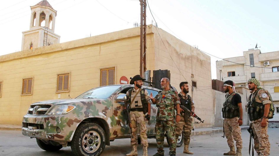 Members of the Assyrian Gozarto Protection Forces (GPF), consisting of Sutoro militia, a pro-government Syriac Christian movement, and other Assyrian fighters chat next to a church before heading to reinforce pro-government forces on the front line in the battle against the Islamic State (IS) group, in the northeastern Syrian province of Hasakeh on July 13, 2015. AFP PHOTO / YOUSSEF KARWASHAN