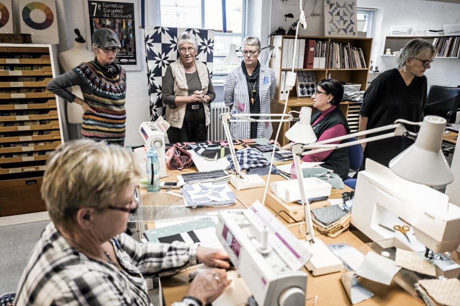 Rundt omkring i lokalet hænger halvfærdige patchworktæpper og afslører kursisternes forskellige stile og smage ud i mønstre og farver.