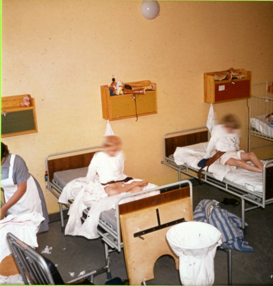 Børneafdeling på åndssvageinstitutionen på Andersvænge. Rutine med bleskift, vask og påklædning. Cirka 1970. (Ansigterne er sløret af redaktionen). –