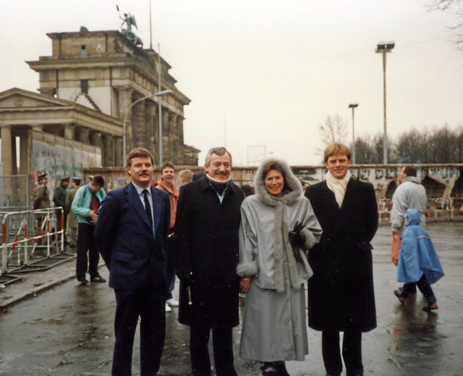 Daværende udenrigsminister Uffe Ellemann-Jensen (V) foran Brandenburger Tor i Berlin februar 1990, hvor Muren stadig står, men glæder sig over dens symbolske fald sammen med sin hustru, Alice Vestergaard, sin chauffør Torben Jørgen (tv.) og ministersekretær Friis Arne Petersen (th.). – Privatfoto.