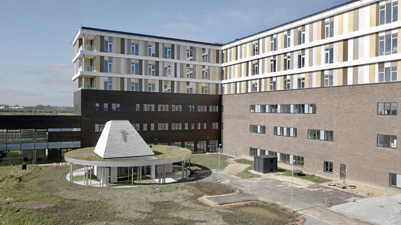 Videre inspirerende fremstår det nye hospital i Gødstrup vel indtil videre ikke – men følges planerne for disponering af det omgivende landskab, vil det med tiden få et grønt udtryk. I forgrunden ses kirkebygningen.