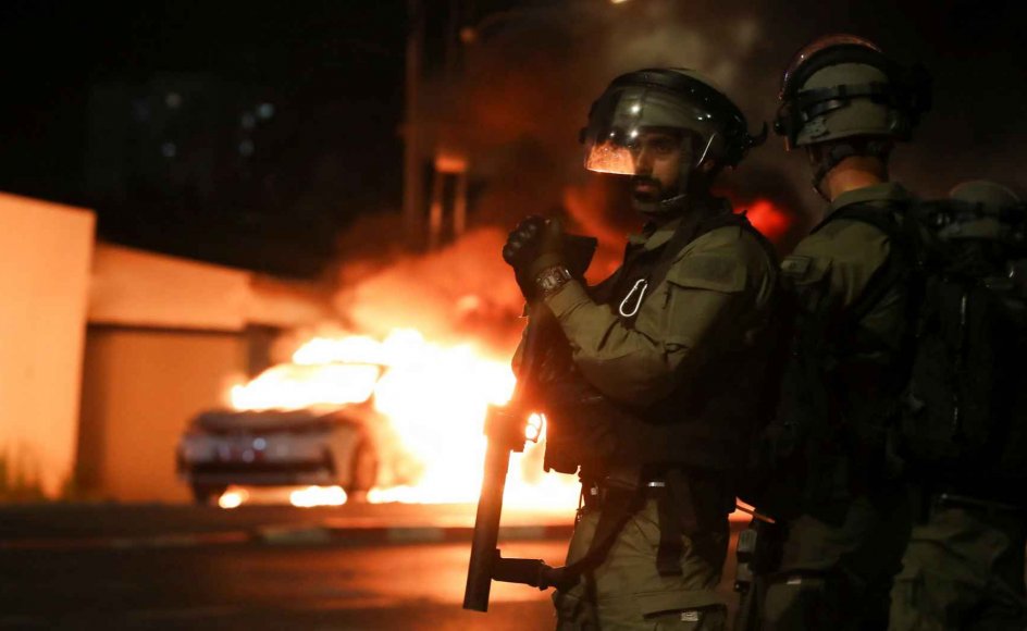 I den israelske by Lod er der erklæret undtagelsestilstand, og fra klokken 20 om aftenen til klokken fire om morgenen er der udgangsforbud. De israelske myndigheder har sendt grænsepolitiet, der under normale forhold er udstationeret i Østjerusalem og på Vestbredden, til byen for at skabe ro. Her ses medlemmer af den israelske sikkerhedsstyrke foran en brændende politibil i byen.