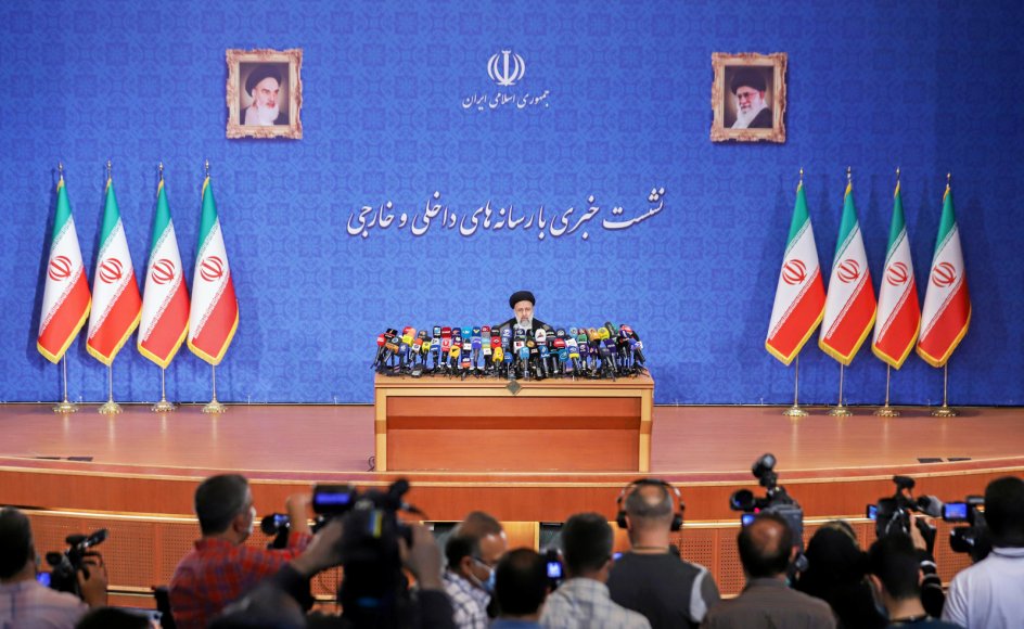 Medier fra hele verden var mødt op, da Ebrahim Raisi i går holdt sit første pressemøde efter valgsejren og straks kritiserede USA foran billeder af ayatollaherne Khomeini og Khamenei (th.).