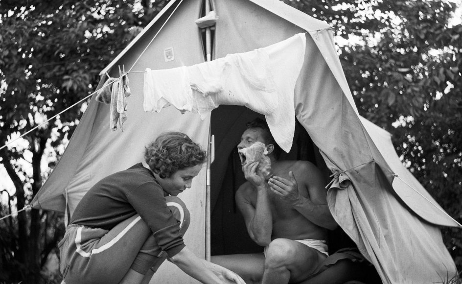 En julidag i 1958 klarer en kvinde opvasken i teltåbningen, mens hendes mand barberer sig. Den primitive ferieform har udviklet sig en del siden.