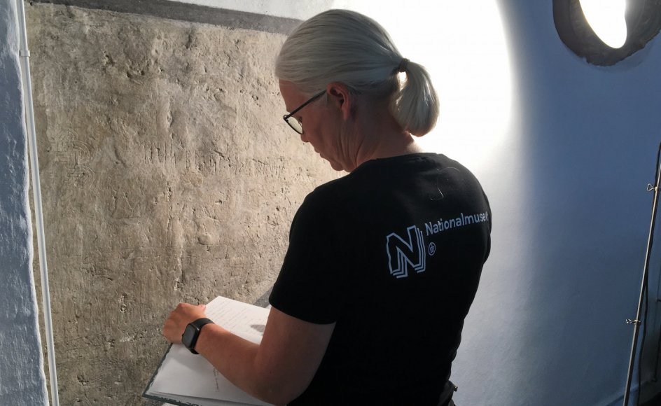 Seniorforsker Lisbeth Imer aftegner indskrifter på den oprindelige vægflade i koret i Tjæreby Kirke. Det vinklede lys får indskrifterne til at træde tydeligt frem.