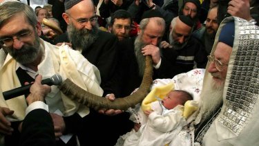 En otte dage gammel dreng bliver båret frem inden sin omskæring af overrabbiner Mordechay Eliyahu i Jerusalem, mens en mand spiller på "shofar," det jødiske vædderhorn.