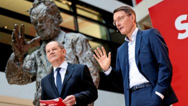 Tysklands nye socialdemokratiske kansler Olaf Scholz (tv.) præsenterede mandag sit ministerhold, herunder den nye sundhedsminister Karl Lauterbach (th.), som skal få skik på landets vaccinekaos, foran bronzestatuen af den legendariske, afdøde kansler Will